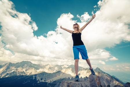 Young lady standing on top of the hill with raised handsの写真素材