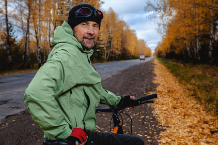 Mature bicycle tourist with his bike on an asphalt autumn roadの写真素材