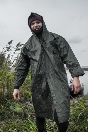 Man in a wetsuit and raincoat stands on the autumn meadow with grassの写真素材