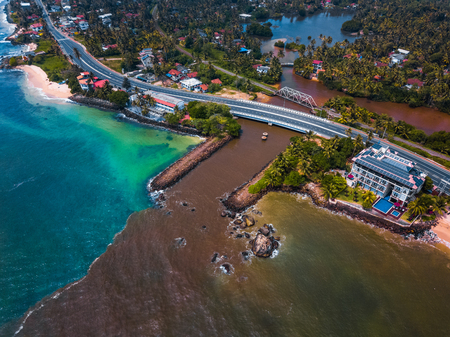 Dirty river flows into clear ocean. Aerial shot of the south coast of Sri Lankaの写真素材