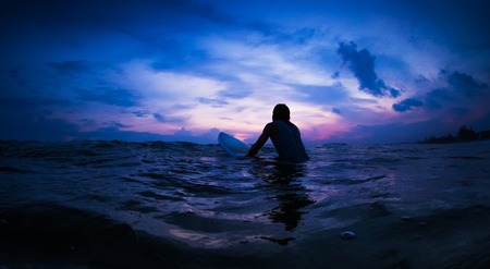 Surfer waits the wave in an ocean during sunsetの写真素材
