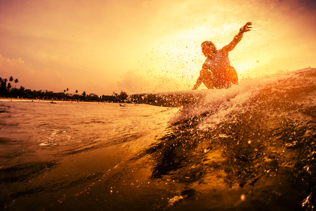 Young surfer rides the wave during sunsetの写真素材