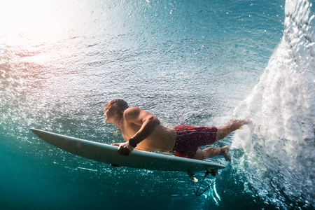 Young surfer dives under the ocean wave and performs trick named in surfing as a Duck Diveの写真素材