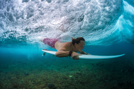 Young surfer make trick named Duck Dive to pass the ocean wave. Extreme sport and active lifestyle conceptの写真素材