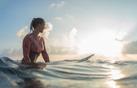 Young lady surfer waits the waves in the ocean during sunriseの写真素材