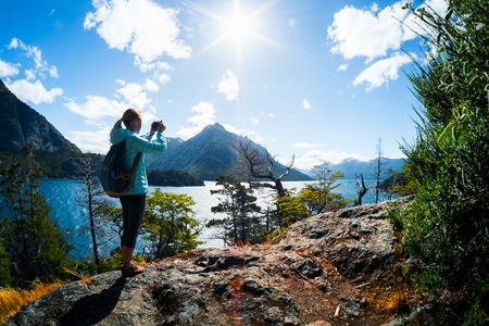 Woman hiker takes a pictures of a valley with lake and mountains. Patagonia, Argentinaの写真素材