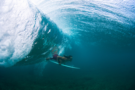 Underwater view of the young male surfer passing the ocean wave with surf boardの写真素材