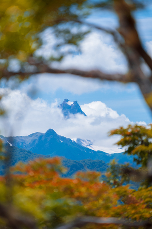 Snow capped mountain covered with clouds and lush trees on the foreground. Patagonia, Chileの写真素材