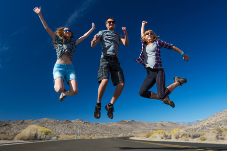 Happy friends jump and have fun on a roadの写真素材