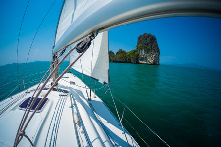 Sailing boat moves under the sails in a tropical sea and aproaches the islandの写真素材