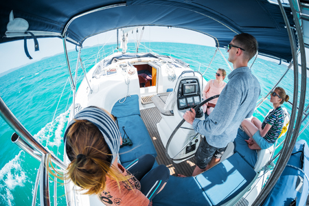 Young captain steers sailing boat in a tropical sea with three young ladies on boardの写真素材