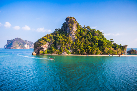 Traditional longtail Thai boat moves in a calm sea near the tropical green island with a beach. Thailandの写真素材