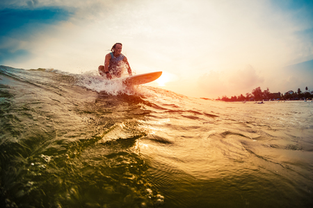 Young surfer rides the wave during sunsetの写真素材