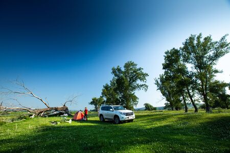 BASHKORTOSTAN, RUSSIA- 25 JULY, 2018: Car travelers camp on the wild, set tent on the perfect green lawn among the trees with car parked nearby.のeditorial素材