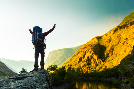 Hiker with backpack stands on the rock with raised hands and enjoys sunrise valley views. Altai, Russiaの写真素材