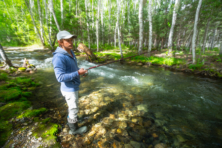 Young amateur angler fishing in the small rapid river in the forest. Altai, Russiaの写真素材