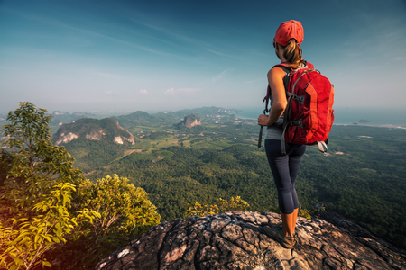 Woman hiker stands on the cliff with backpack and watches the walleyの写真素材