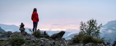 Panorama with lady hiker standing on top of the mountain among stacked stones and enjoying sunset over the valley. Altai, Russiaの写真素材