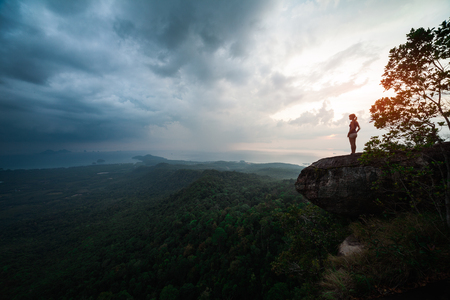 Woman stands on the cliff and enjoys the valley view during sunsetの写真素材