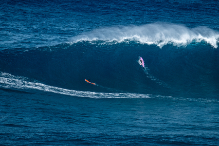 Two big wave surfers paddle to line up and pass huge ocean wave of Jaws (Peahi) surf spot on Maui, Hawaii.の写真素材