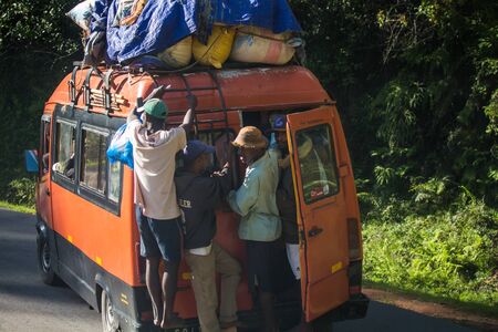 ANTSIRABE / MADAGASCAR - 23 DECEMBER 2013: Passengers hang outside the crowded loaded bus with open back doorのeditorial素材