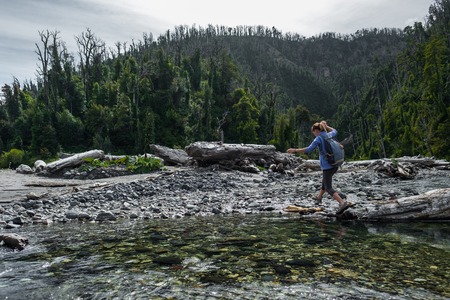 Woman hiker crossing the small river in the wild areaの写真素材