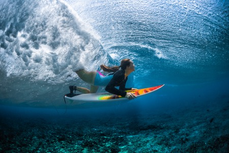 Underwater shot of the young woman surfer diving under the wave with her surfboardの写真素材
