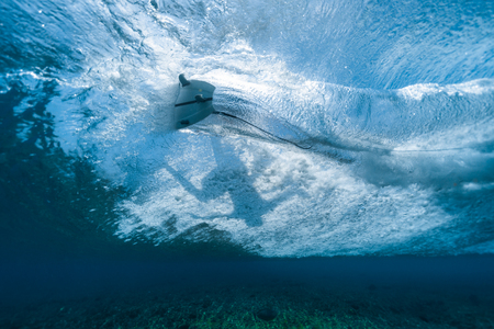 Underwater view of the surfer riding the crystal clear ocean wave and making sharp turnの写真素材
