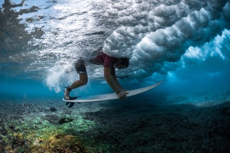 Surfer dives under the wave with the surfboard to safely pass it and performs the Duck Dive trickの写真素材