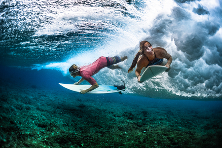 Two young surfers man and woman survive under the breaking ocean waveの写真素材