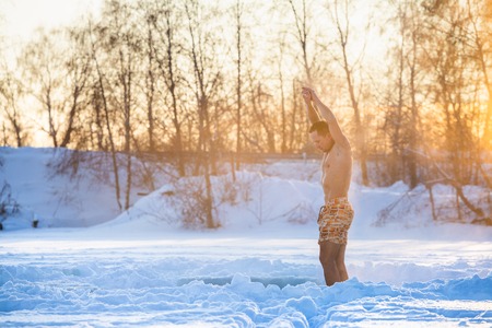 Semi naked man does exercises and meditates in the winter field with sun shining through the treesの写真素材