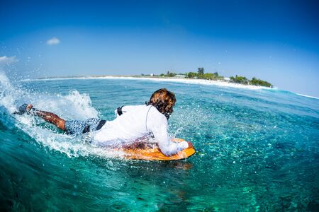 MALDIVES / HIMMAFUSHI - 08 MARCH 2019: Local maldivian surfer rides the blue ocean wave on bodyboard