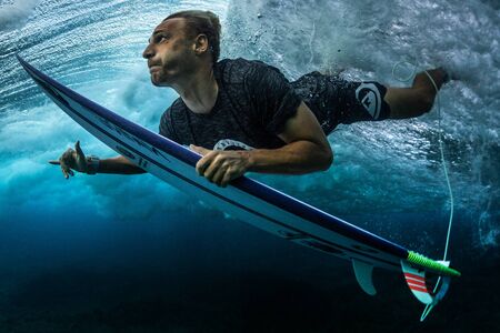 MALDIVES / HURAA - 23 MARCH 2019: Male surfer dives under the wave with his surfboard and shows the...