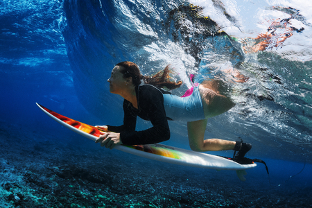 Underwater shot of the young woman surfer diving under the wave with her surfboardの写真素材