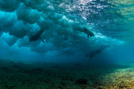 Underwater photographer takes photo of the female surfer diving under the waveの写真素材