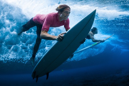 Surfers dive under the breaking waveの写真素材