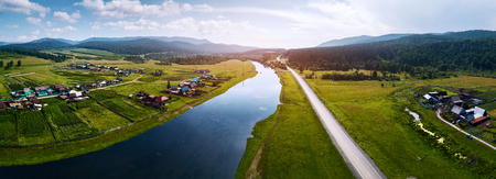 Aerial panorama of the river of Belaya with the villages on its green coasts, asphalt road along the river and Ural Mountains on the horizonの写真素材