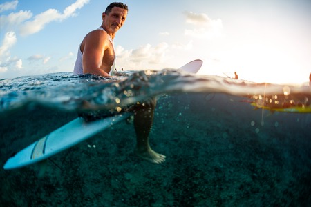 Adult male surfer sits on his board and looks at the camera
