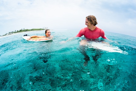 Two young and happy surfers have fun in the ocean - man sits on the board and woman swims and look...