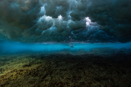 Surfer swims underwater on the shallow reef area in the waveâs impact zoneの写真素材