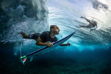 MALDIVES / HURAA - 23 MARCH 2019: Male surfer dives under the wave with his surfboard and shows the Shaka signのeditorial素材