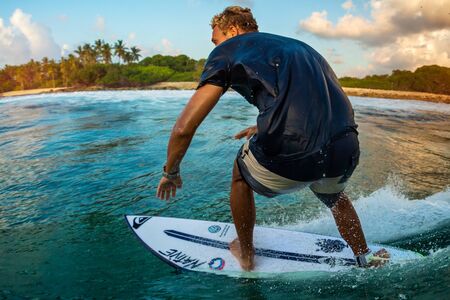 MALDIVES / HURAA - 22 MARCH 2019: Professional surfer rides ocean wave at Honkeys surf spot during sunset surf sessionのeditorial素材