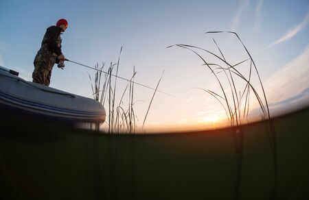 Amateur angler fishing from the boat on the lake at sunsetの写真素材