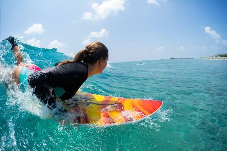 Young woman surfer takes off and starts riding the ocean tropical wave. The surf spot named Chickens in Maldivesの写真素材