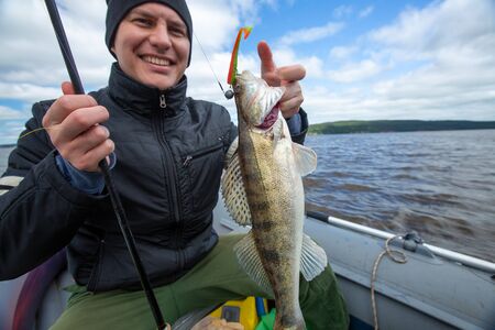 Young happy amateur angler holds the fish (Zander) in the hand being on the lake