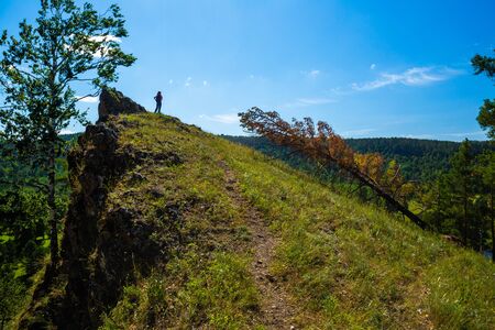 Hiker with backpack stands on top of the hill at sunny dayの写真素材