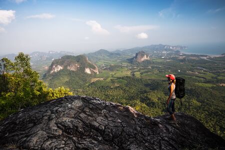 Woman hiker with backpack stands on the rock and observes the valleyの写真素材