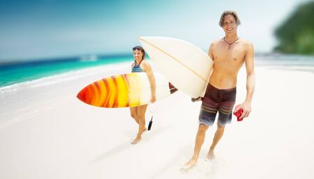 Two happy caucasian surfers walk on the sandy beach with their surboards. Blurred backgroundの写真素材