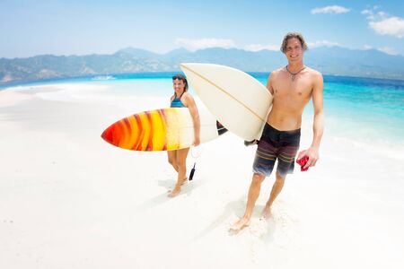 Two happy caucasian surfers walk on the sandy beach with their surboards after surfingの写真素材