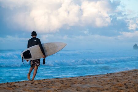 OAHU / USA - NOVEMBER 13, 2019: Surfer walks along the beach with his surfboard. Seven Mile Miracle on The North Shore of Oahu, Hawaiiのeditorial素材